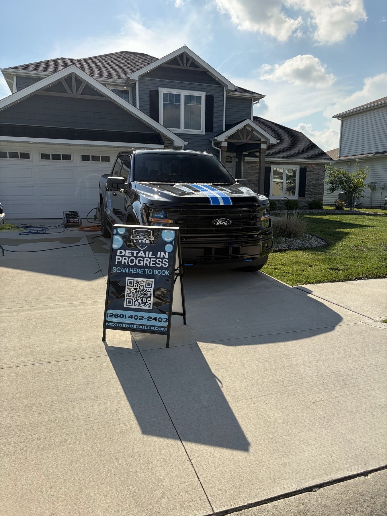 Black Ford F-150 with blue racing stripes detailed in a customer driveway, NextGen sign out front