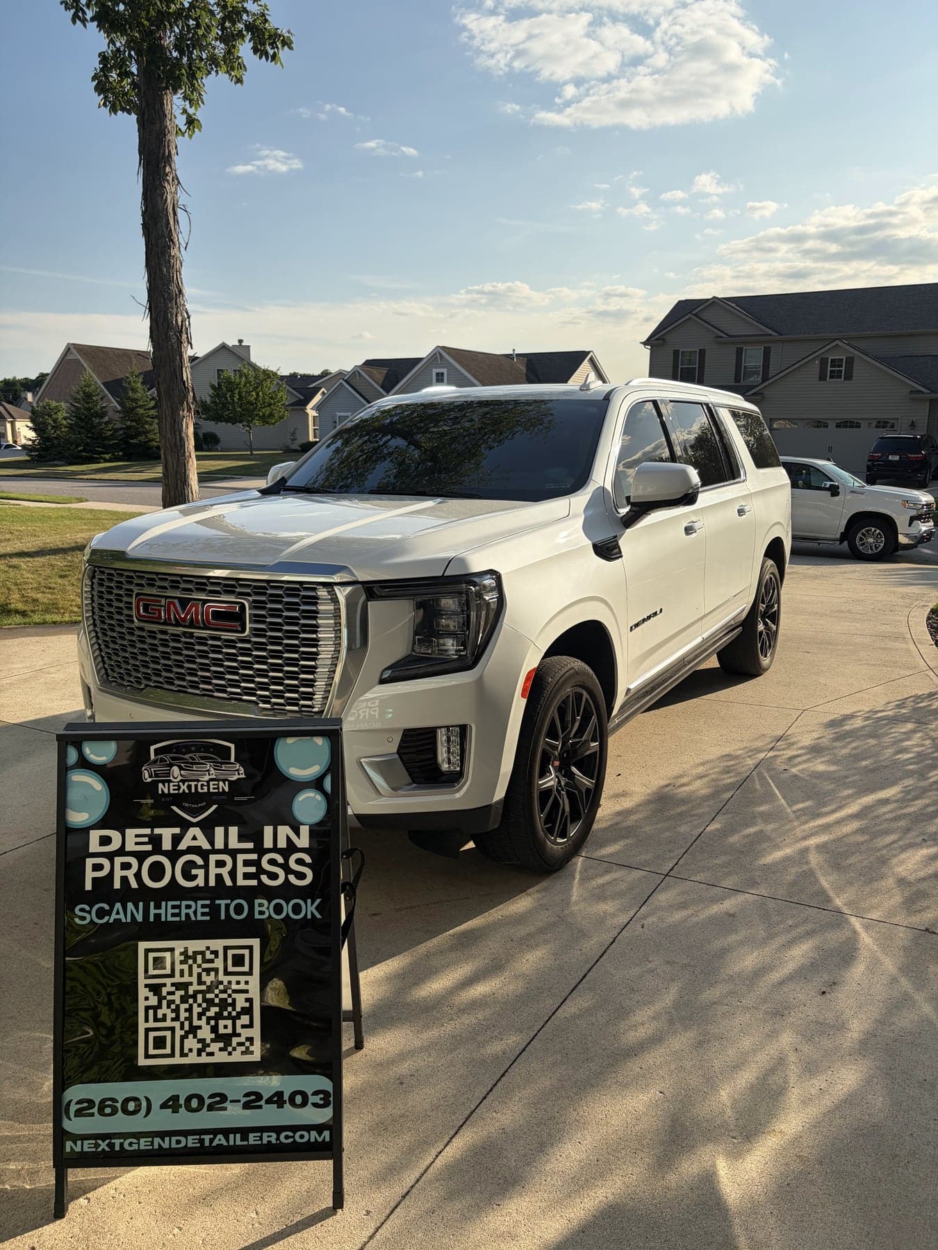 White GMC Yukon Denali freshly detailed in a customer driveway, NextGen sign out front