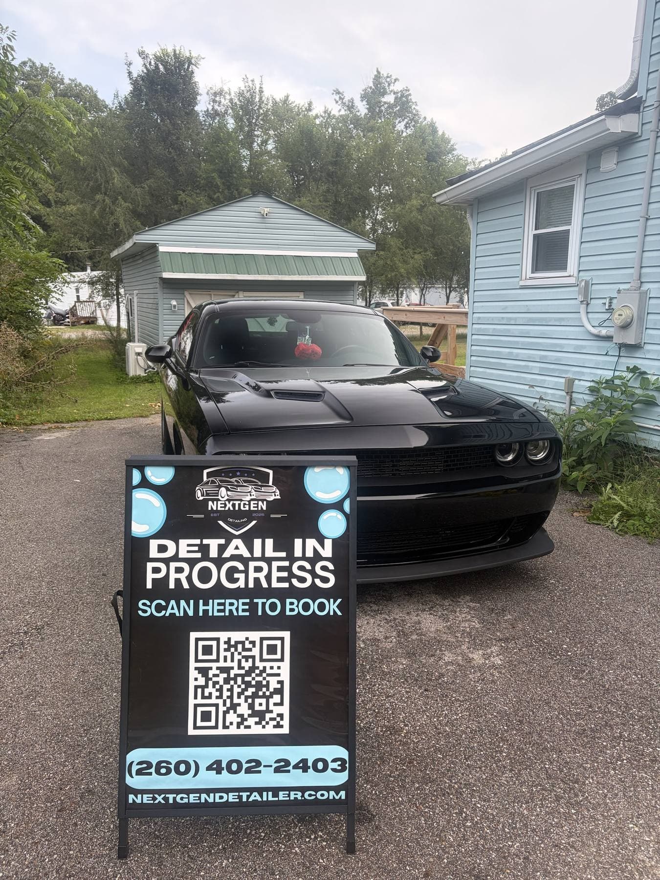 Black Dodge Challenger freshly detailed in a customer driveway, NextGen Detail in Progress sign out front